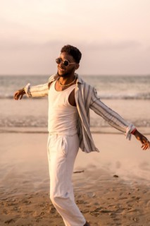 Portrait of attractive black ethnic man enjoying summer vacation by the sea feeling free and dancing