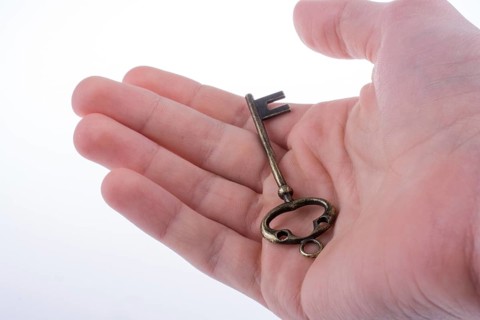 Hand holding a retro styled metal key on a white background