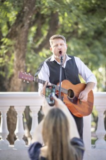 Street musician performing at a park and a girl from the audience taking pictures and filming him