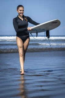 Young woman with prosthesis coming out of the sea with her surfboard. Concept of disability in sport