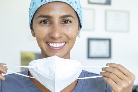 Beautiful doctor smiles at the camera while removing her mask