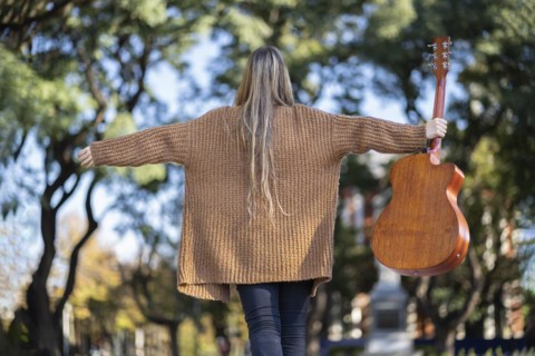 Guitarist in a park posing backwards holding his guitar with one hand