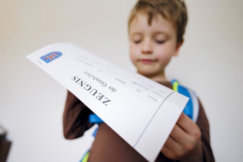 Symbolic photo on the subject of report cards in primary school. A boy poses with a report card. Berlin