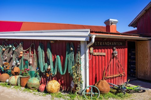 Discarded maritime objects and equipment such as rusty buoys and old fishing nets displayed on the wooden wall of a shed