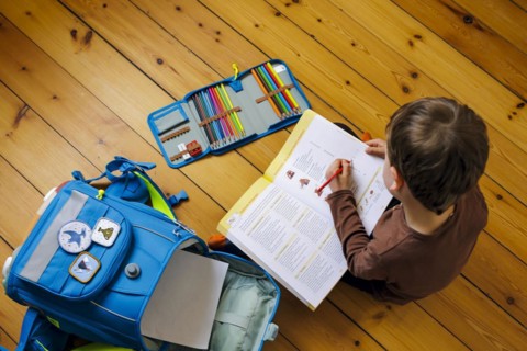 Symbolic photo on the subject of doing homework at home. A boy sits on the floor doing homework. Berlin