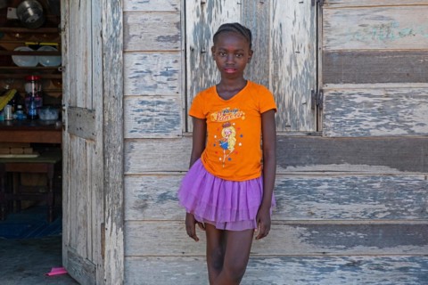 Portrait of young Afro-Surinamese girl with braided hair in front of wooden house in the village Aurora
