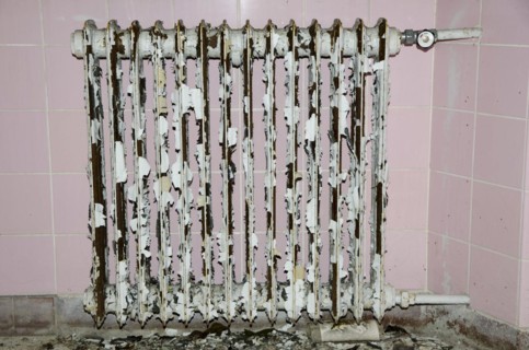 Old rusty radiator with pink tiles in background