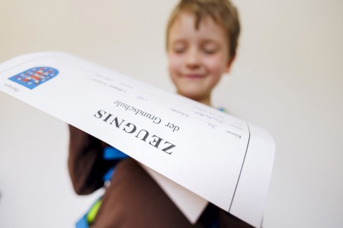 Symbolic photo on the subject of report cards in primary school. A boy poses with a report card. Berlin