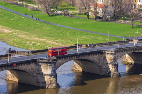 A red double-decker bus of a local city tour company crosses the Augustusbruecke
