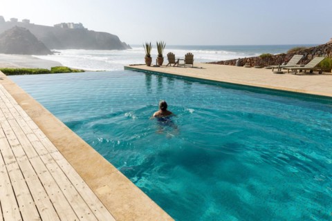 Woman swimming infinity pool by Atlantic Ocean