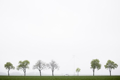 A car is silhouetted against wind turbines on a country road in Vierkirchen