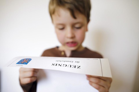 Symbolic photo on the subject of report cards in primary school. A boy poses with a report card. Berlin
