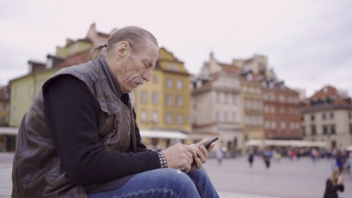Senior sits on the steps and uses a smartphone in the historic center of an old European city
