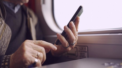 Close-up of the hands of an senior sitting in a train carriageriage and using a smartphone