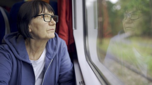 Elderly lady in glasses travels in train and looking out the window reflected in the glass