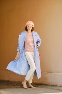 Playful woman standing in arch and waiving her blue trench coat
