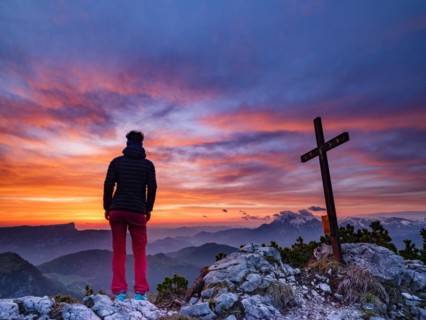 Mountaineer next to the summit cross of the iceberg and red clouds at dawn