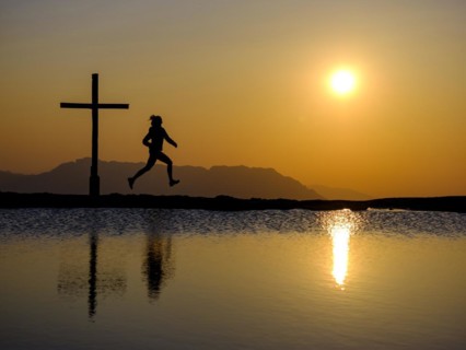 Silhouette of a runner with summit cross at sunset