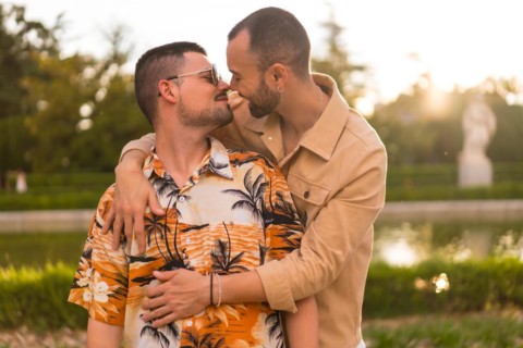 Homosexual couple embracing giving each other a kiss looking at the sunset in a park in the city