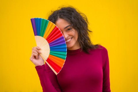 Portrait of a latin woman smiling with a rainbow lgbt fan on a yellow background