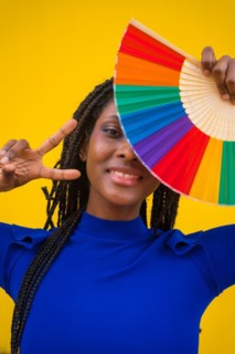A black ethnic woman with a rainbow lgbt fan on a yellow background