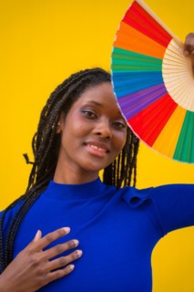 Portrait of an attractive black ethnic woman with a rainbow lgbt fan on a yellow background