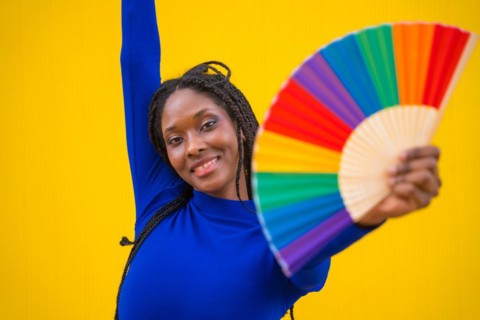 Portrait of an attractive black ethnic woman with a rainbow lgbt fan on a yellow background