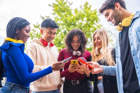 Low angle view of a group of young multi-ethnic teenage friends using cell phones on campus in the city