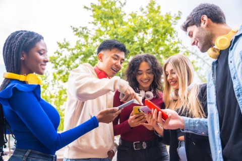 A group of young multi-ethnic teenage friends using cell phones in the city campus