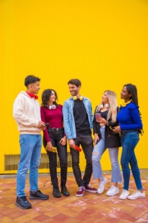 Portrait of a group of smiling young multi-ethnic teenage friends using cell phones on a yellow background