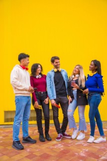 Portrait of a group of smiling young multi-ethnic teenage friends using cell phones on a yellow background