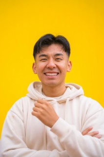Portrait of a handsome South Korean Asian man in basic clothes smiling isolated over yellow background