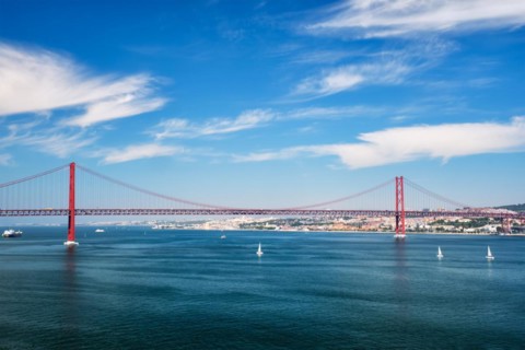 View of 25 de Abril Bridge famous tourist landmark of Lisbon connecting Lisboa to Almada on Setubal Peninsula over Tagus river with boats yachts and vessels
