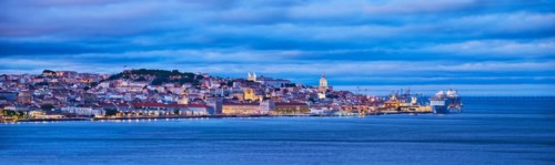 View of Lisbon over Tagus river with passing ferry boat from Almada with moored cruise liner in evening twilight