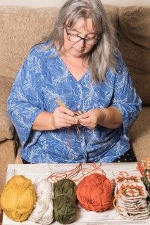 Front view of an older woman with white hair and glasses crocheting with her wool in the foreground