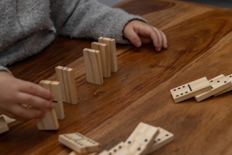 Child's hands in gray sweater playing dominoes with blurred focus