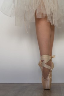 Legs of girl dancing ballet with tulle skirt and pink shoes different dance steps wooden floor and white background with copy space