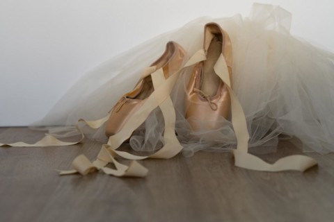Ballet slippers with orange ribbon on a wooden floor and white background