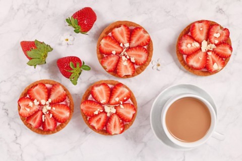 Small tartlet pastries topped with strawberry fruits and white chocolate sprinkles next to coffee cup