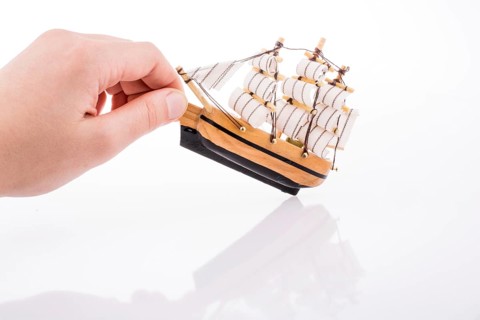 Hand in touch with a little model sailboat on a white background