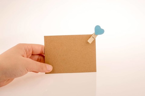 Hand holding a paper placed in a clothespin withe heart on a white background