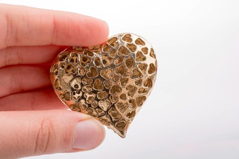 Heart shaped gold color metal object in hand