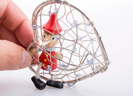 Wooden Pinocchio doll sitting in a heart shaped cage