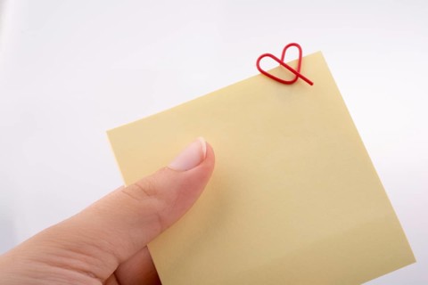 Hand holding a notepaper heart shaped clip on a white background