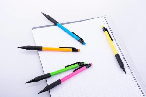 Mechanical pencils of various color on a notebook on white background