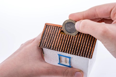 Hand dropping coin into the moneybox in the shape of a model house