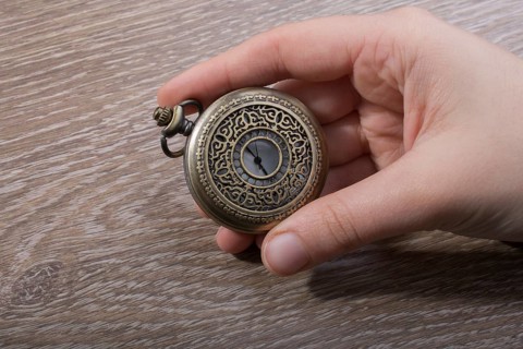 Retro style pocket watch in hand on black background
