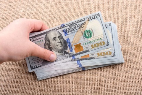 Hand holding banknote bundle of US dollar on a linen canvas background