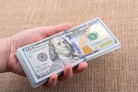 Hand holding banknote bundle of US dollar on a linen canvas background