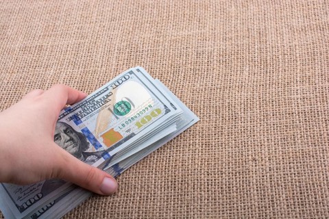 Hand holding banknote bundle of US dollar on a linen canvas background